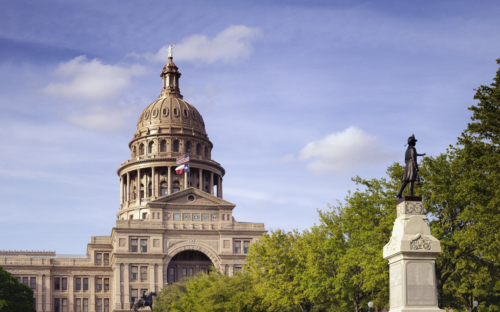 The dome and south front of the Texas state capitol in Austin, seen above trees on a clear spring day