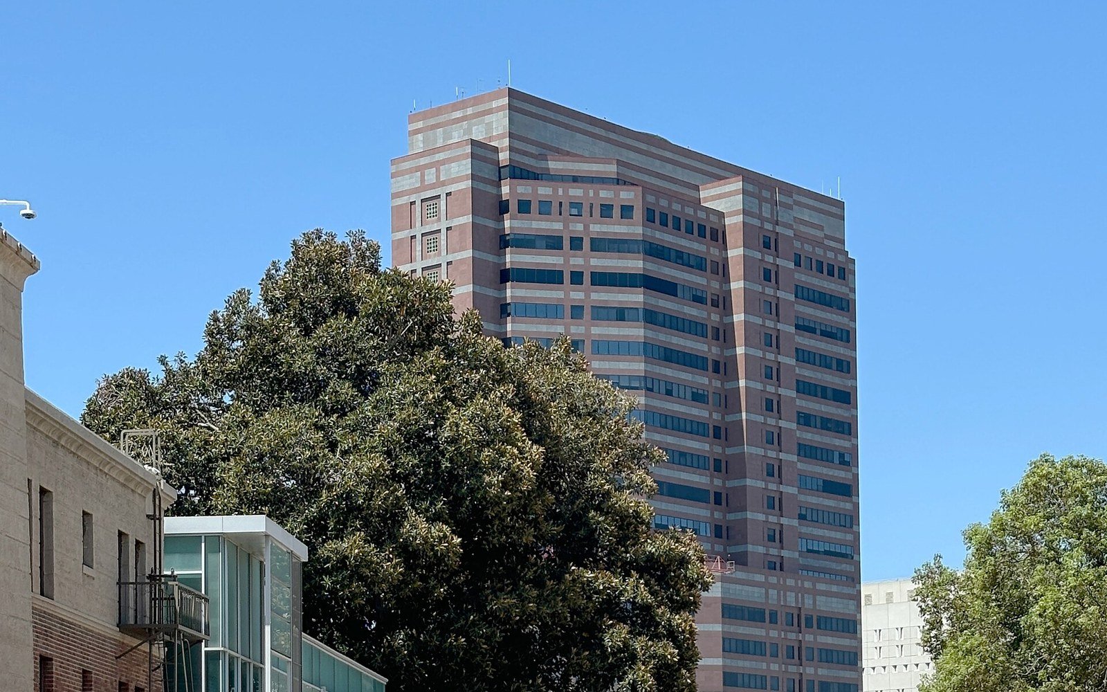The upper storeys of the Edward R. Roybal Federal Building and United States Courthouse in Los Angeles rising above trees against a clear sky