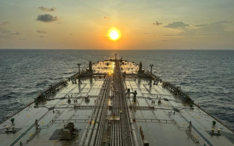 The deck and pipework of a large oil tanker at sea with the sun low on the horizon
