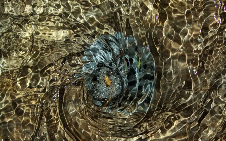 A vortex forming in rippling water, the surface catching light in gold and grey as it spirals inward