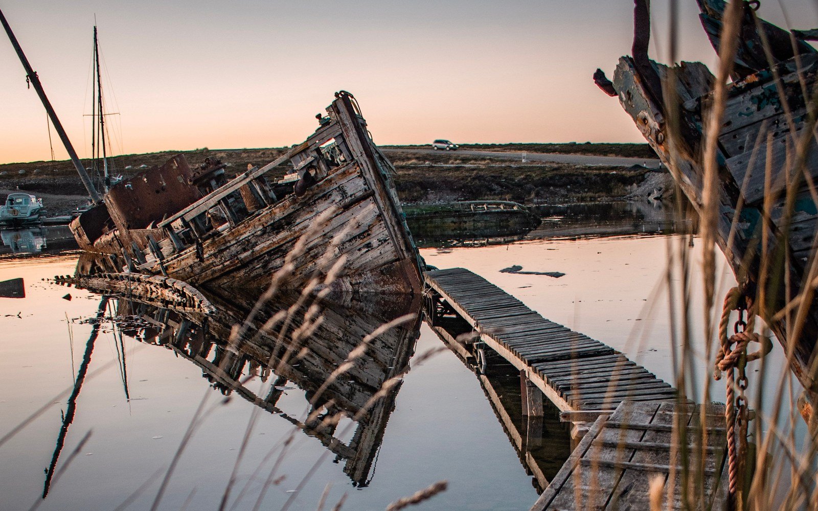 A wooden wreck lying over on its side beside a timber jetty in still water at sunset in Stanley, Falkland Islands