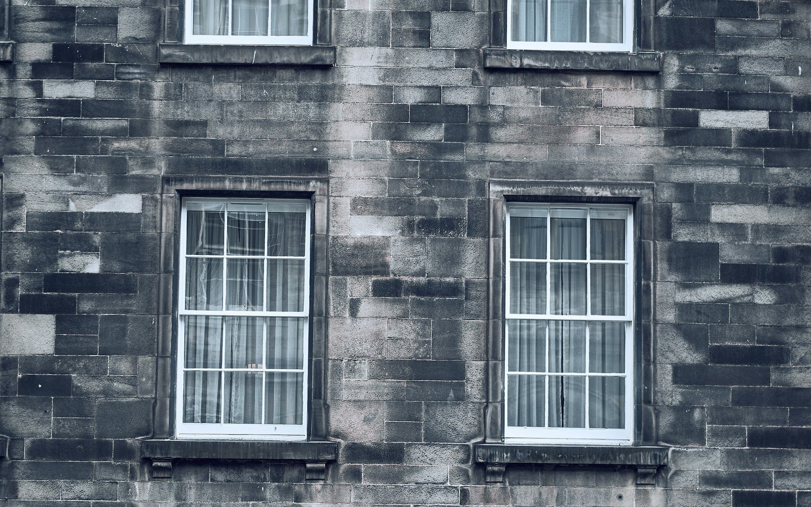 Six white painted sash windows set in the weathered grey ashlar elevation of an old stone building, arranged in two ranges over three storeys