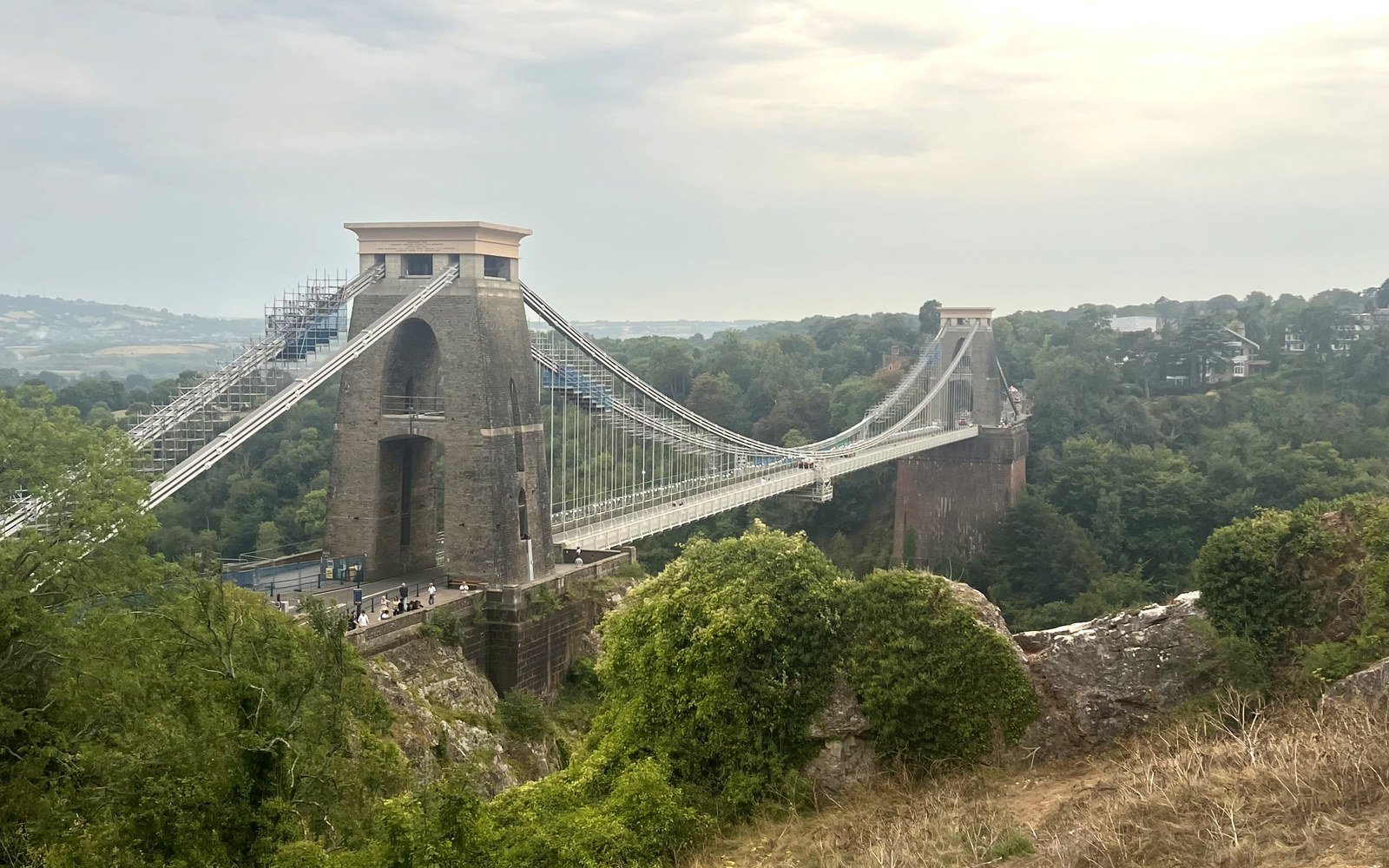 The Clifton Suspension Bridge spanning a wooded gorge between two stone towers under a pale sky