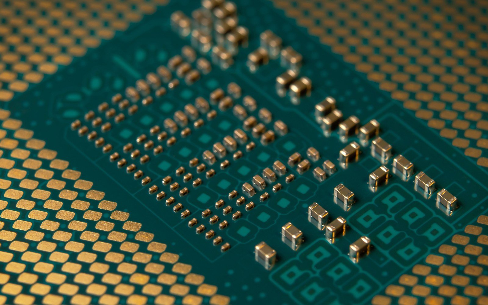A macro view of a green circuit board, rows of gold contact pads and small capacitors filling the frame