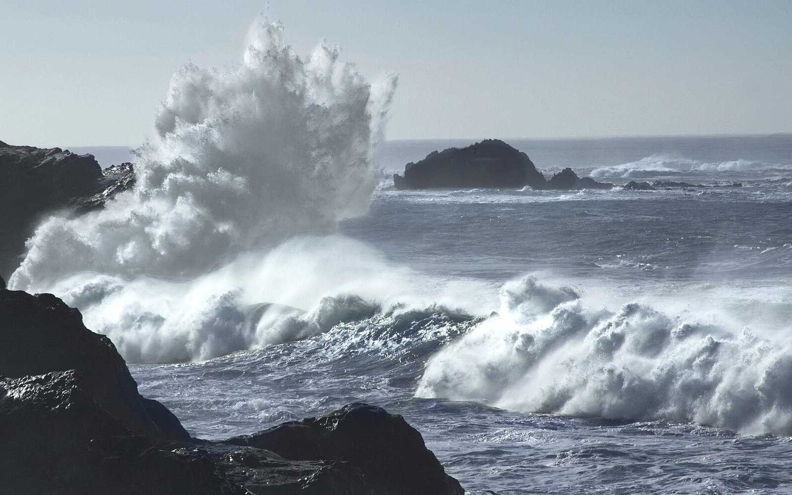 Storm waves breaking over black rocks on the Oregon coast of the Pacific under a pale sky