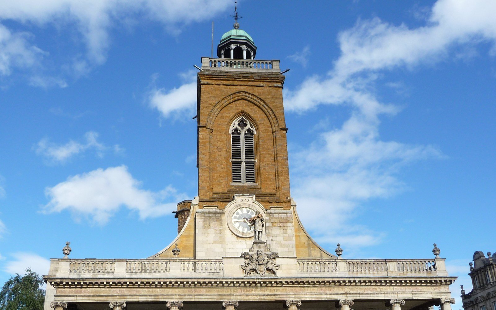 A sandstone church tower with a green cupola and a clock above a classical portico, against a blue sky with white cloud
