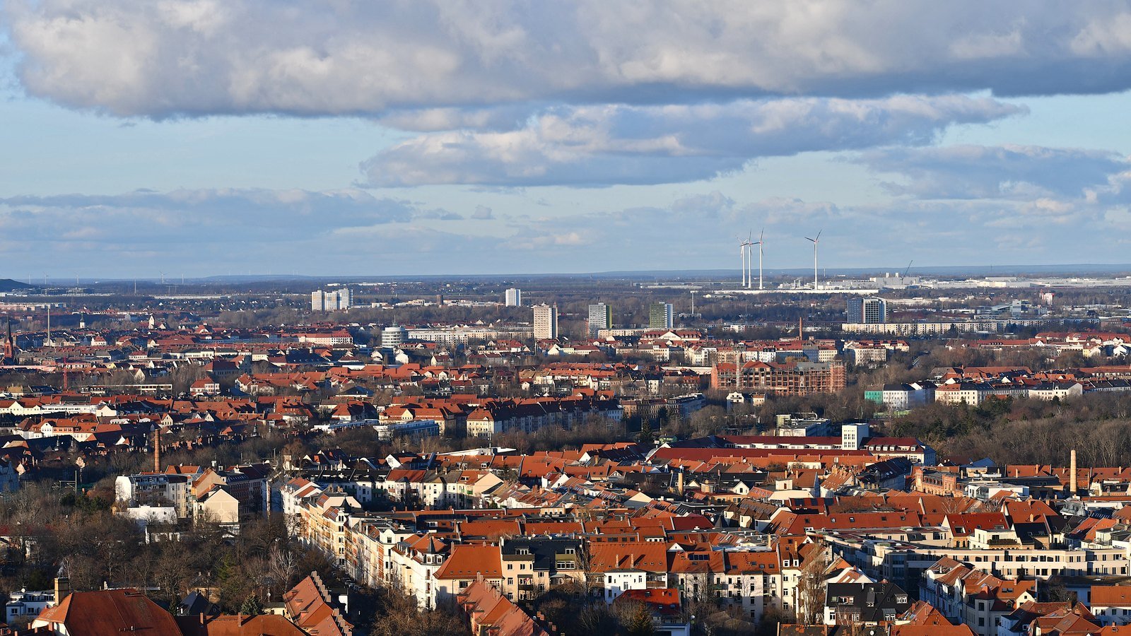 A wide view over the rooftops of Leipzig with wind turbines on the far horizon