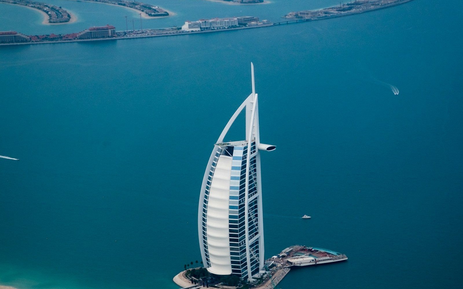 Aerial view of the sail-shaped Burj Al Arab hotel on its island off the Dubai shore, turquoise sea around it