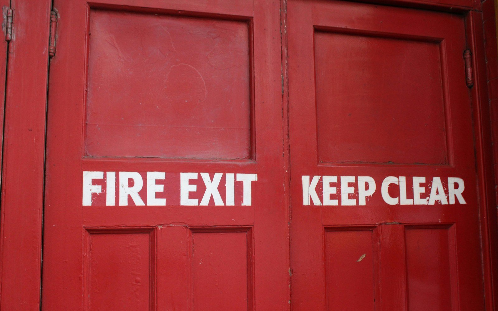 A pair of red-painted panelled fire exit doors with the words fire exit and keep clear stencilled in white across them