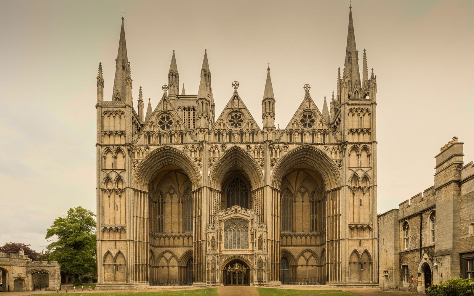 The west front of Peterborough Cathedral in evening light, its three tall Gothic arches flanked by turrets and spires
