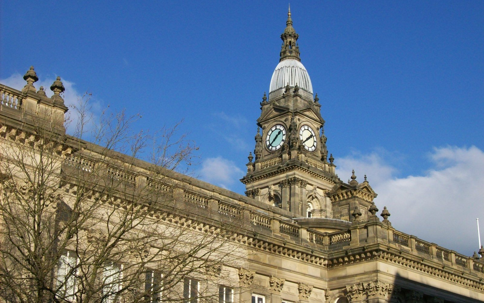 The clock tower and stone facade of Bolton Town Hall against a clear blue sky