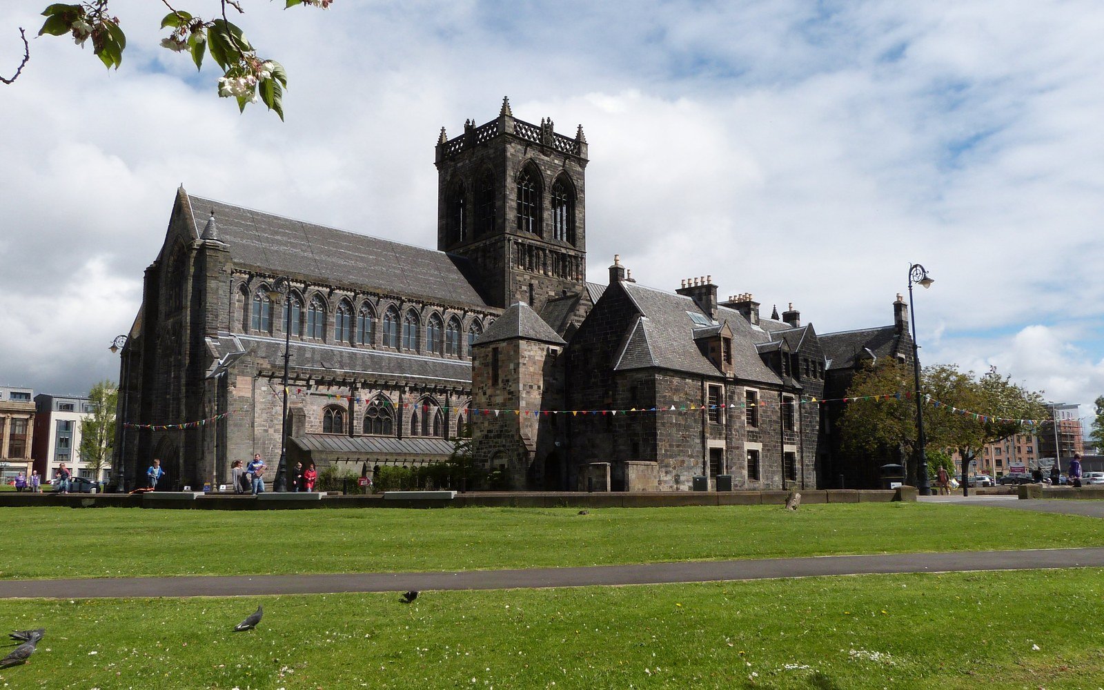 Paisley Abbey, a grey stone church with a square tower and buttressed nave, seen across a mown lawn under a cloudy sky