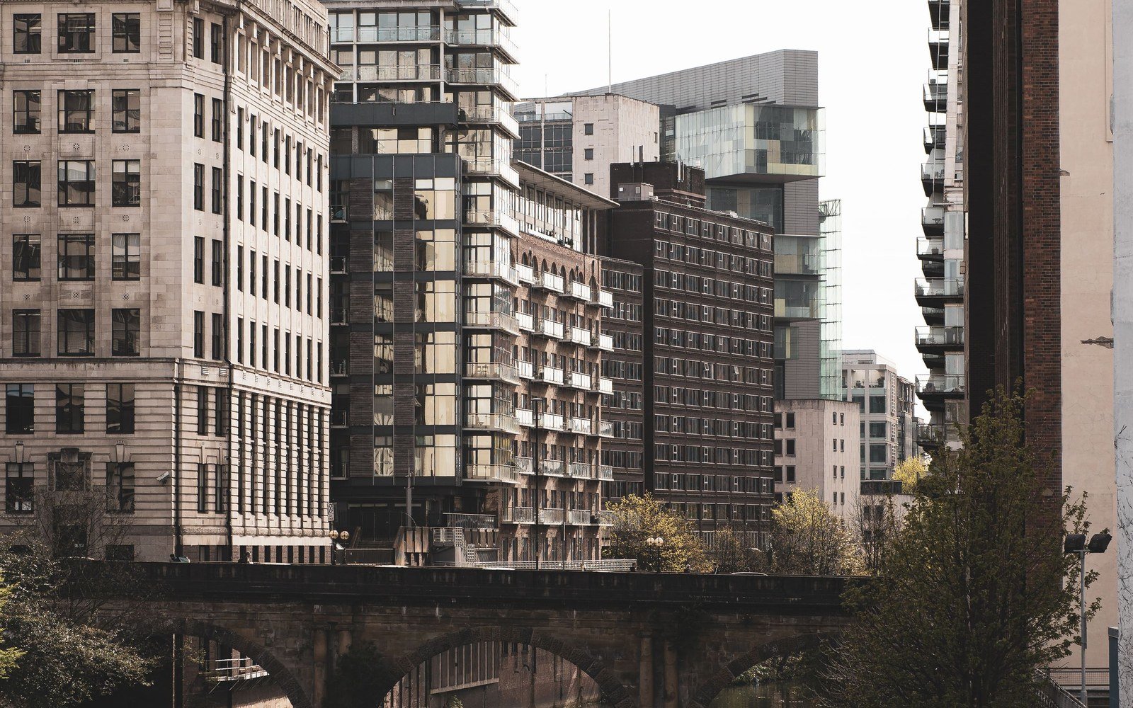 Modern apartment blocks and older stone office buildings rising above a stone railway viaduct in Manchester