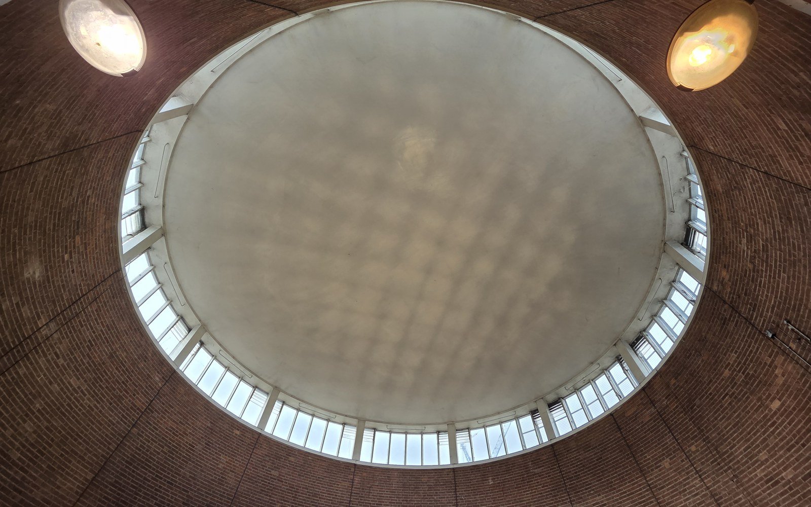 A circular skylight set in a brick domed ceiling, ringed by small windows, with two pendant lamps either side