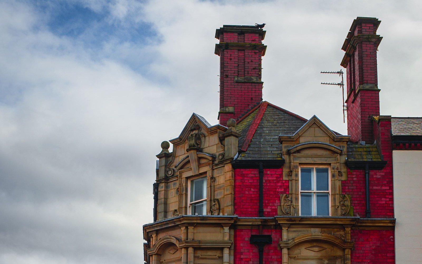 The upper storeys of a Victorian red brick and sandstone building in Liverpool, with carved stone dormers and twin chimney stacks against cloud