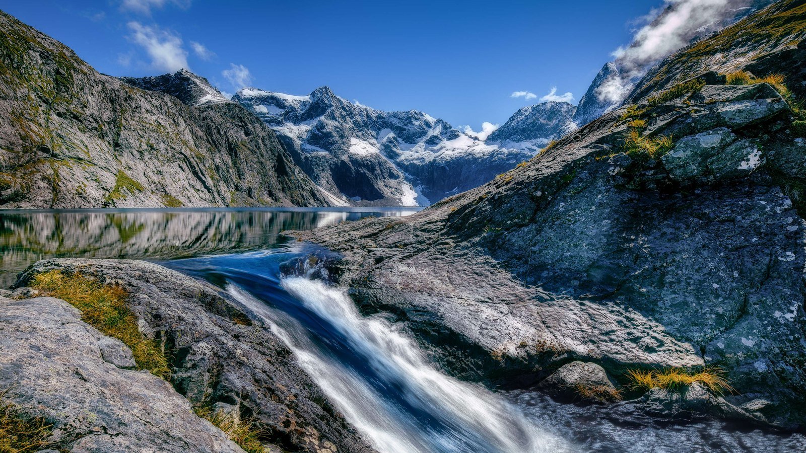 A meltwater stream running between rock slabs below snow covered peaks in Fiordland National Park in New Zealand