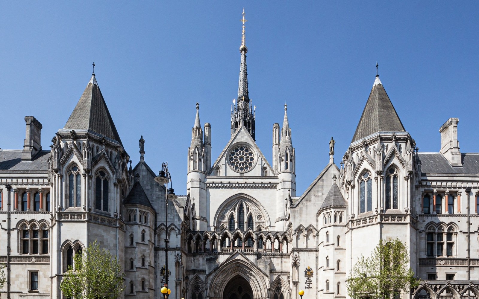 The stone west front of the Royal Courts of Justice in London, with its rose window, gabled porch and central spire against a clear blue sky