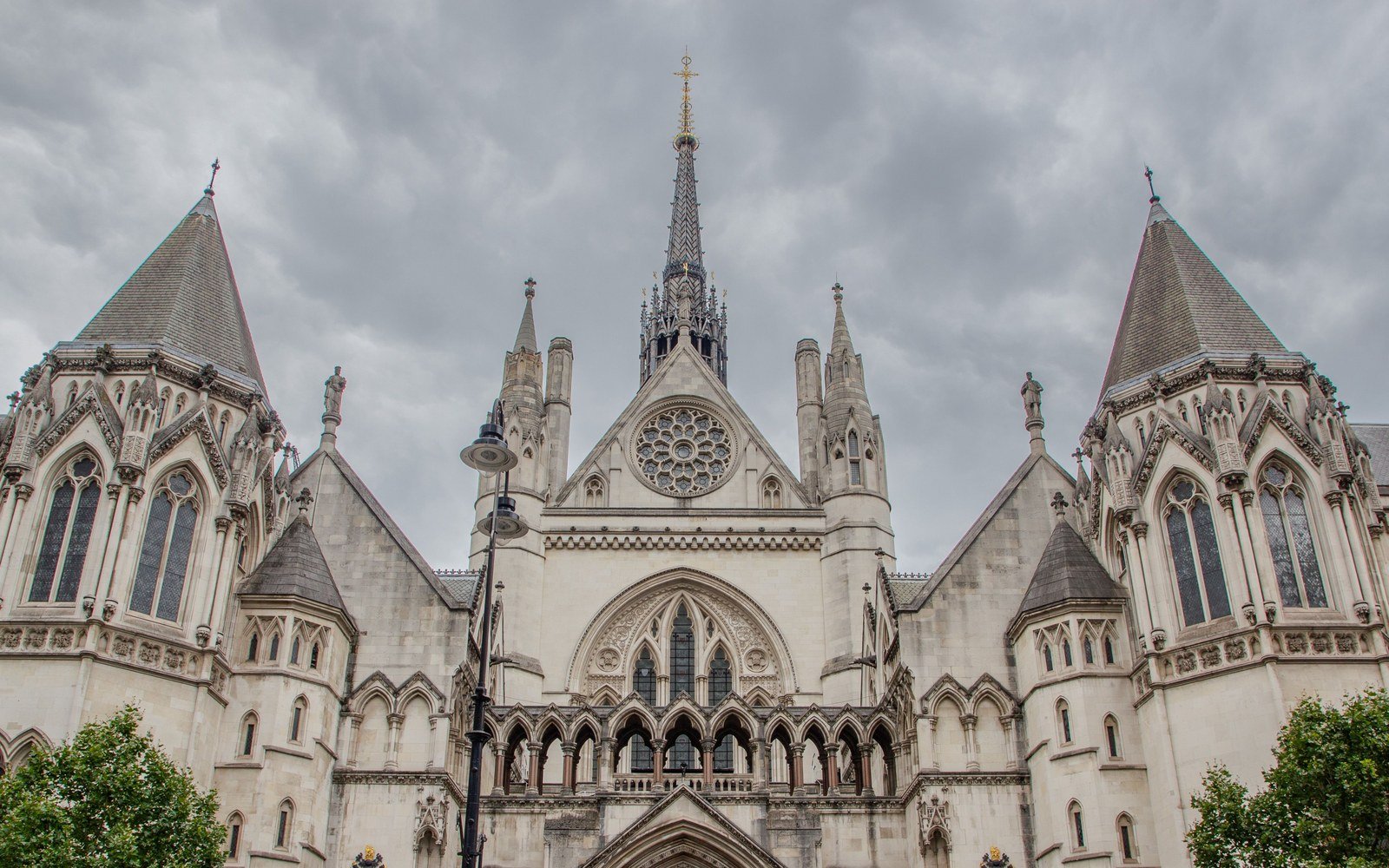 The Gothic stone front of the Royal Courts of Justice in London with its central spire, rose window and twin turrets under a grey sky