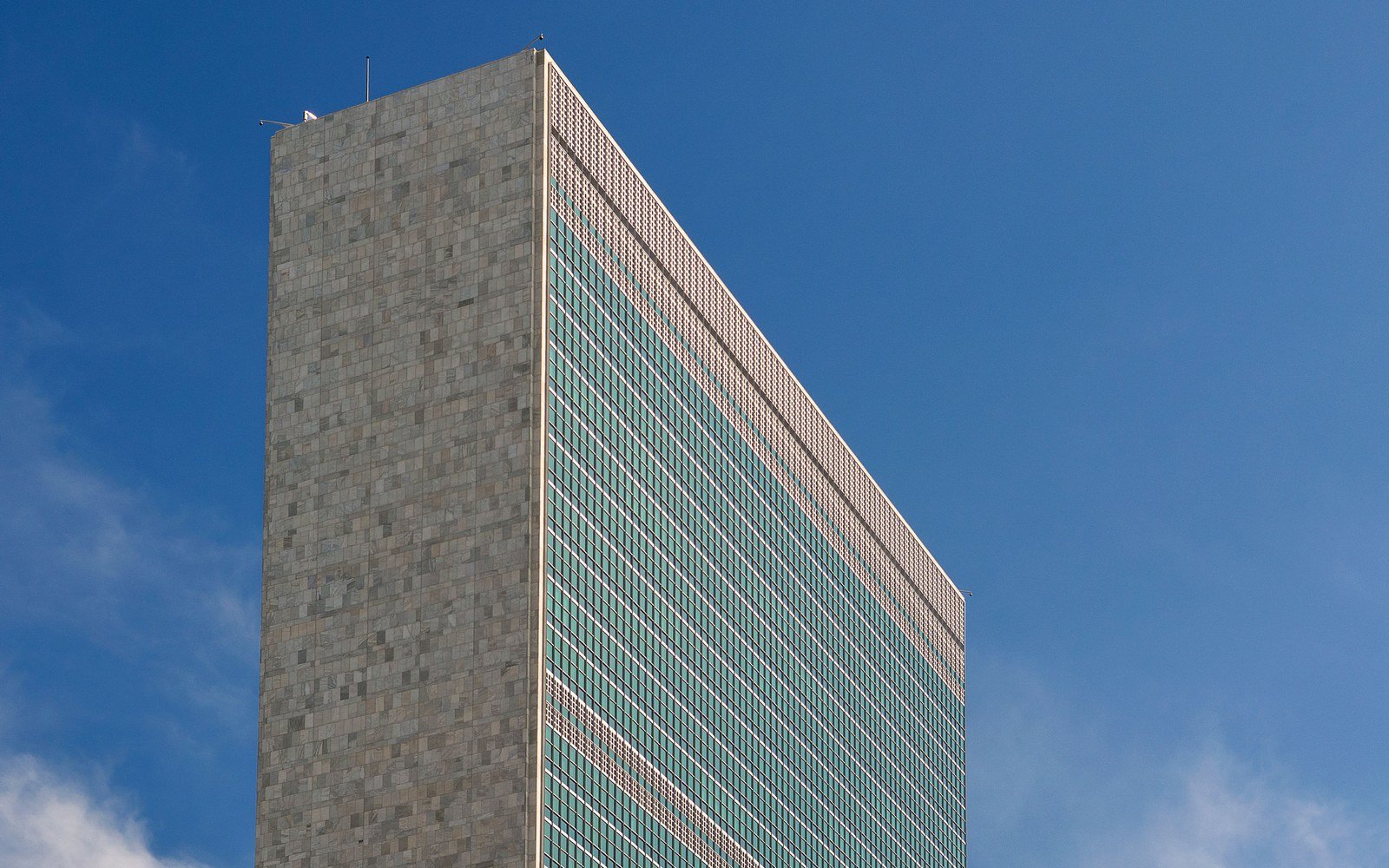 The tall glass and stone slab of the United Nations Secretariat building against a clear blue sky in NYC