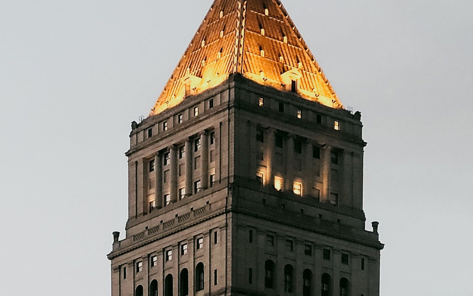 The pyramid topped tower of a federal courthouse in Lower Manhattan lit gold against a grey dusk sky