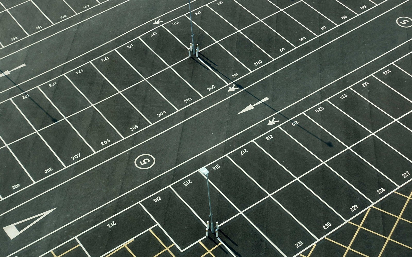 An empty asphalt car park seen from above, laid out in rows of bays marked with white lines, each bay carrying a painted number, with painted arrows on the access lanes