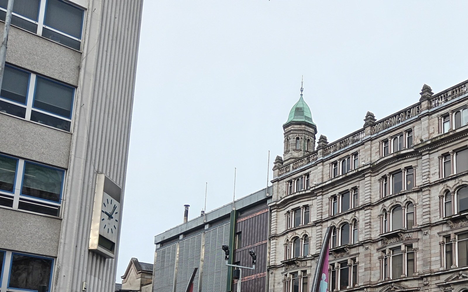 A domed Victorian corner building in pale stone facing a modern office block across a city street