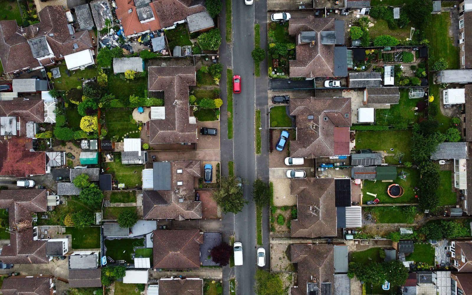 An overhead view of a suburban street of detached and semi detached houses with pitched roofs, back gardens, garages and parked cars