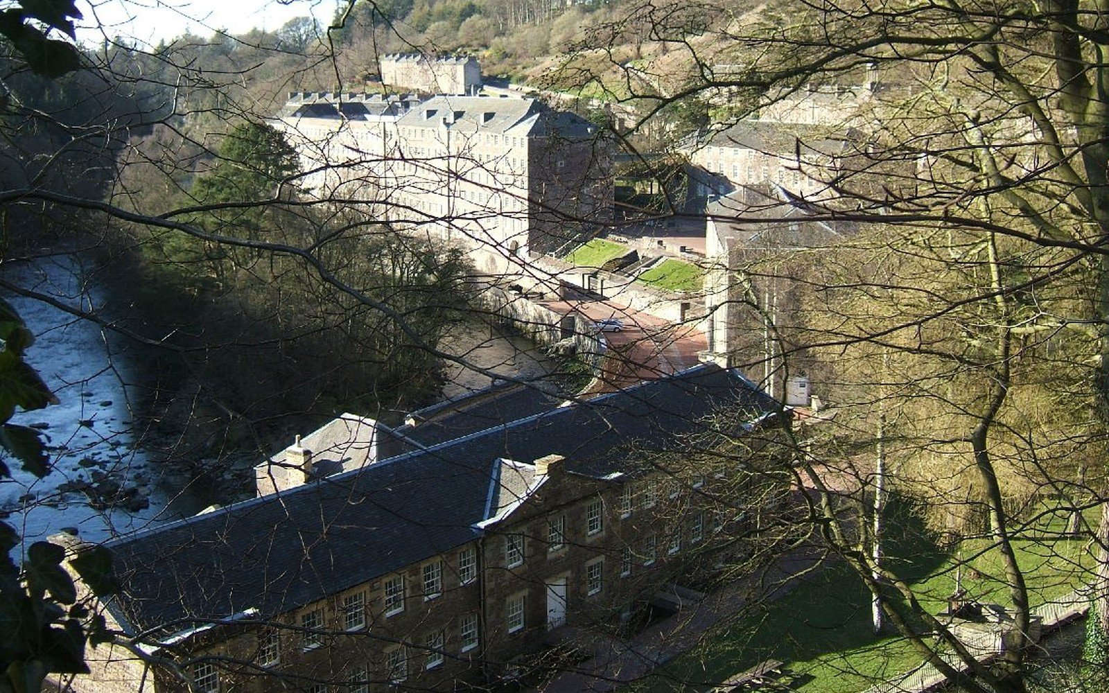 Long stone residential terraces with slate roofs in a wooded river gorge, framed by bare branches