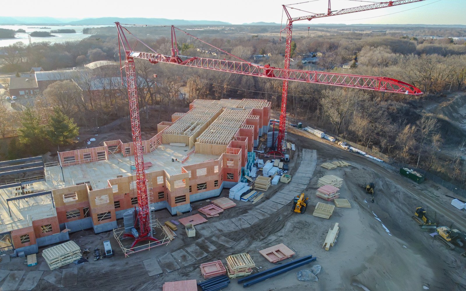 An aerial view of a residential building under construction, with two red tower cranes standing over a part completed timber and concrete frame