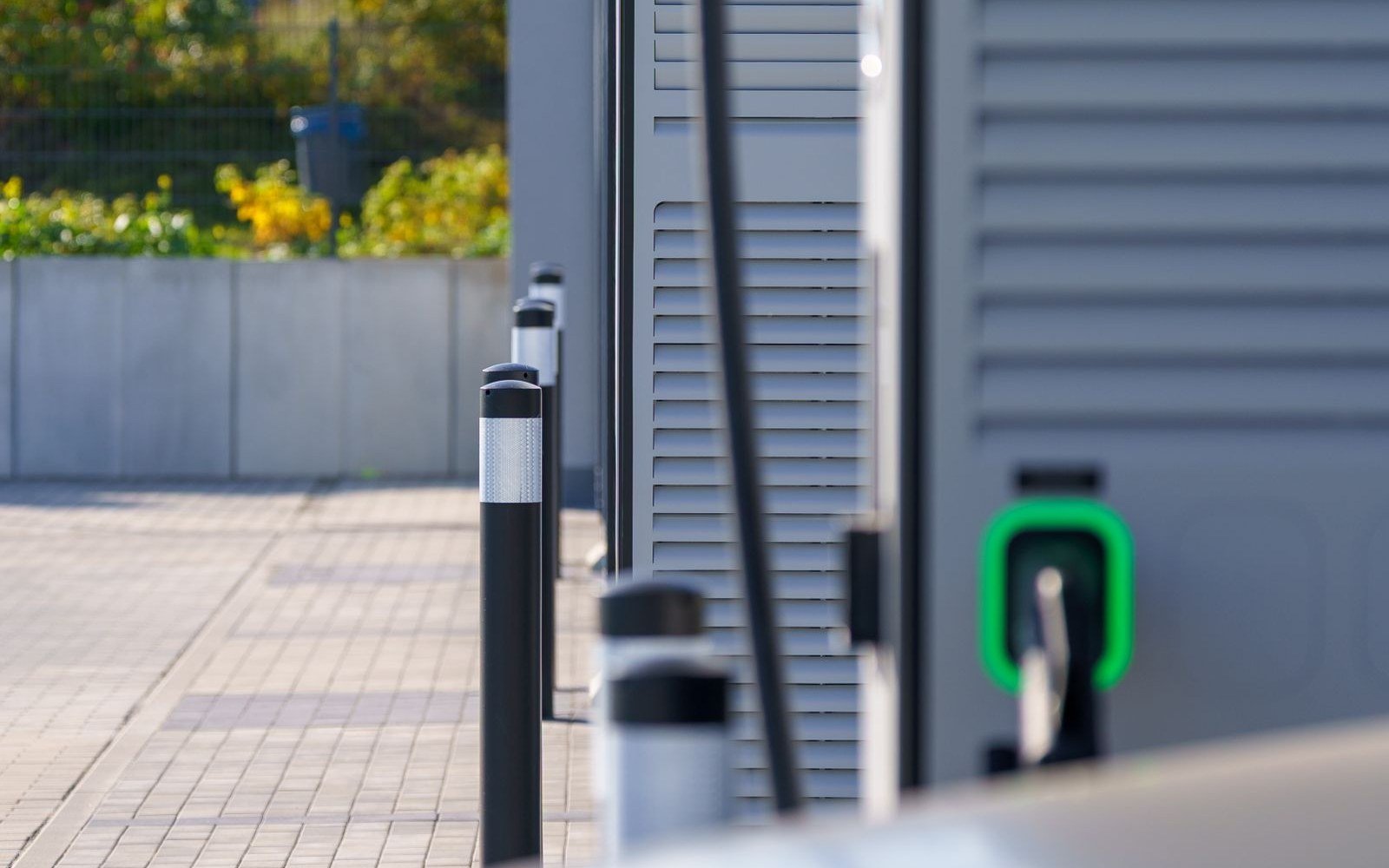 A row of grey electric vehicle charging units with a green indicator light on a paved forecourt
