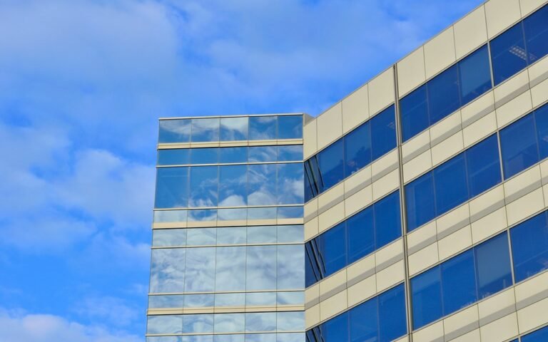 The glazed and cream panelled corner of a modern office block against a blue sky with white clouds