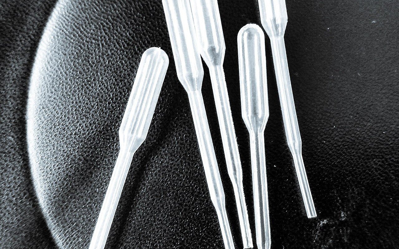 Five clear plastic laboratory pipettes laid on a dark surface