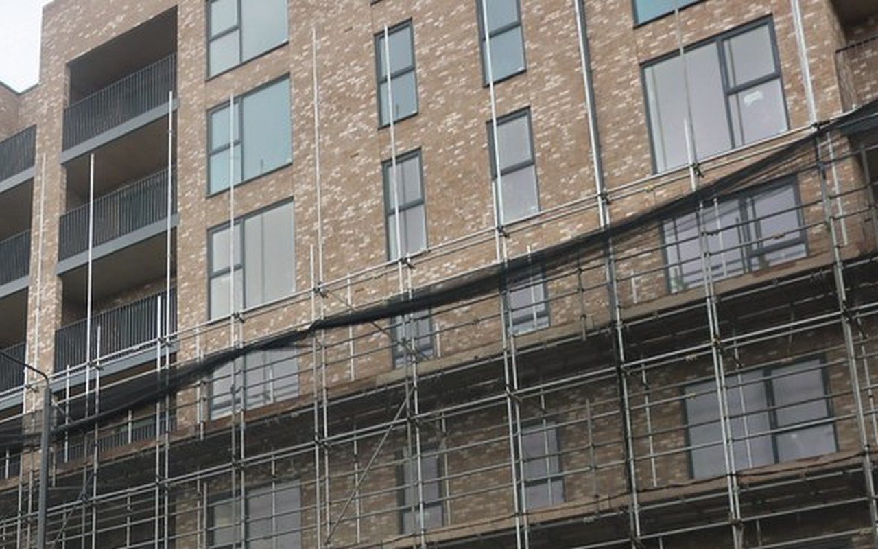 Upper floors of a new brick block of flats with balconies, wrapped in scaffolding at the front
