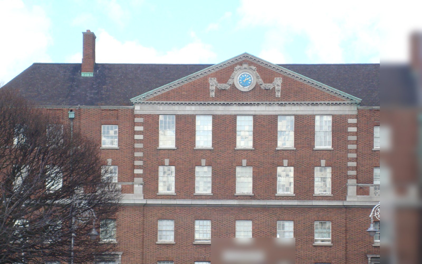 The upper floors of a red brick Georgian revival building with white stone dressings, a pediment with a round clock and rows of sash windows