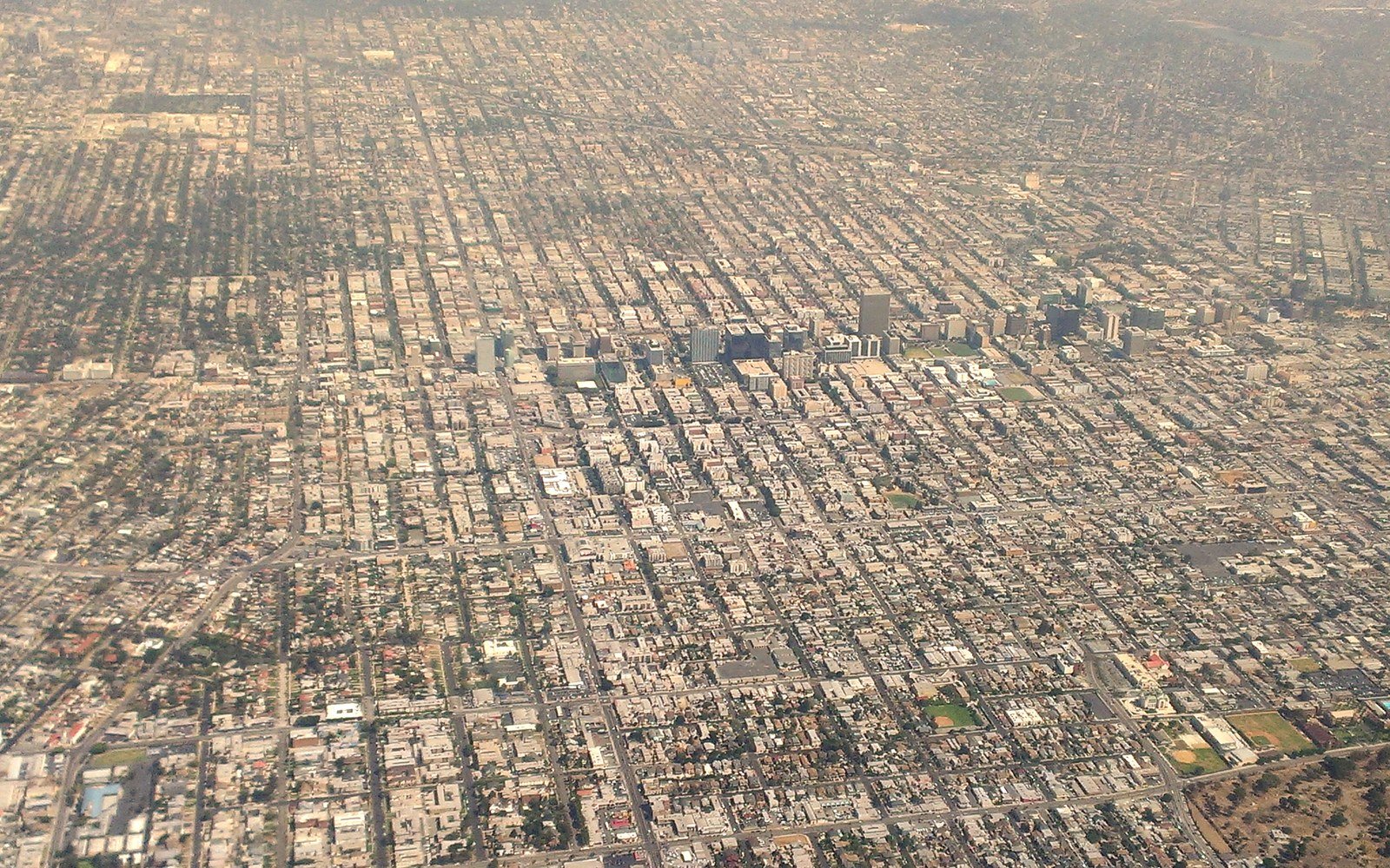 An aerial view over a flat city grid of low buildings and streets stretching to a hazy horizon, with a cluster of taller blocks in the middle distance