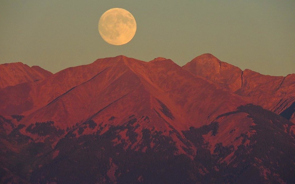 A full Moon rising above a mountain ridge lit red by the setting sun