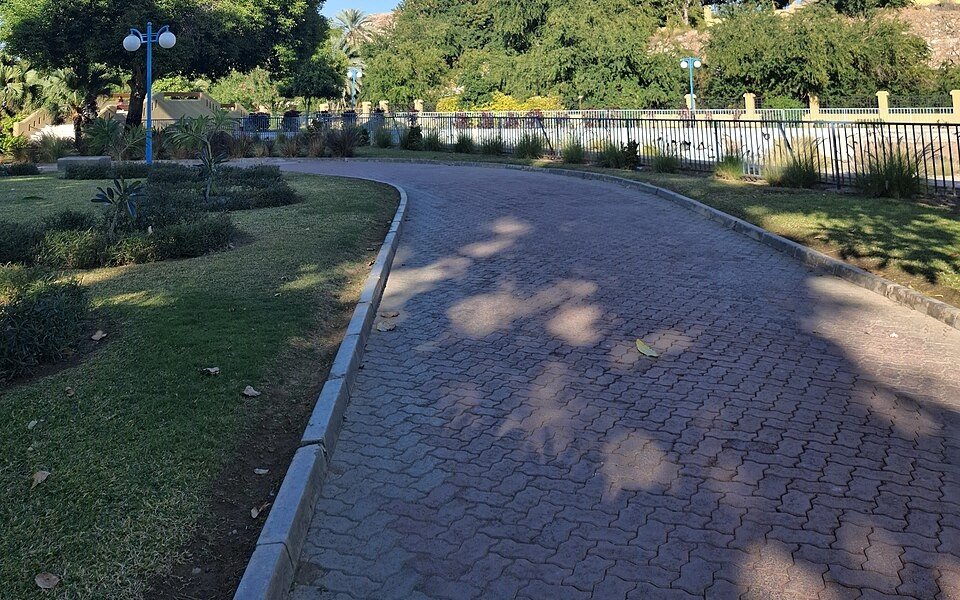 A paved footpath curving between lawns, shrubs and trees in a landscaped public park