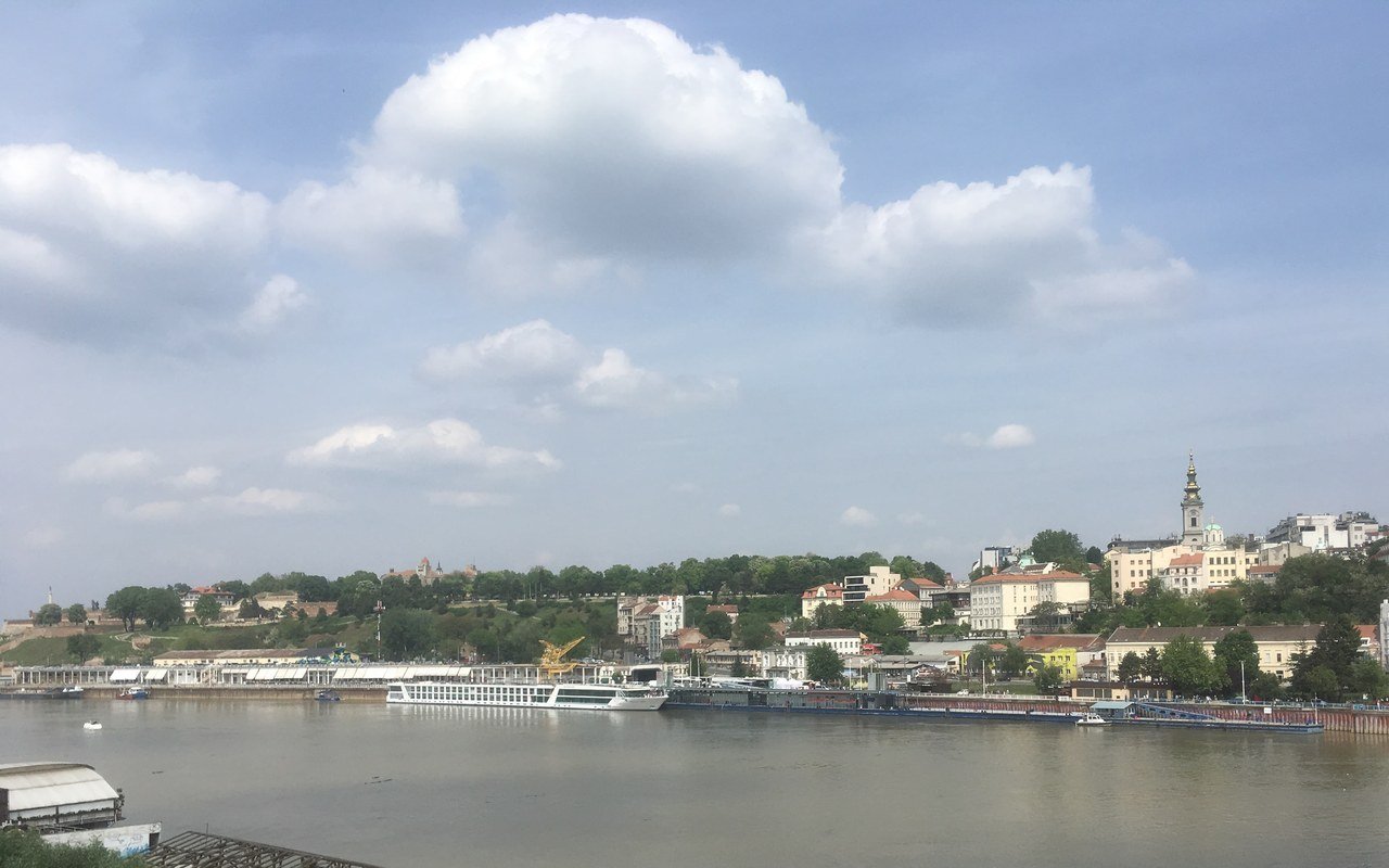 The old town of Belgrade above the River Sava, with a cathedral tower, riverside buildings and a moored river cruise ship under a cloudy sky