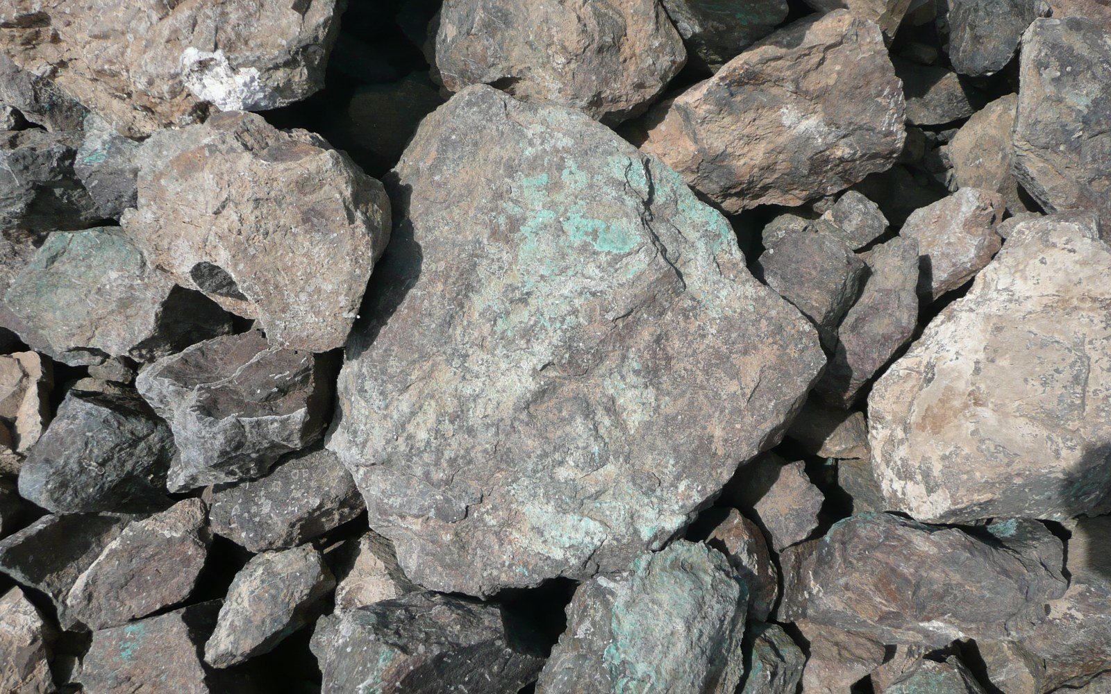 A close view of a heap of large broken grey rocks with green copper staining on their surfaces