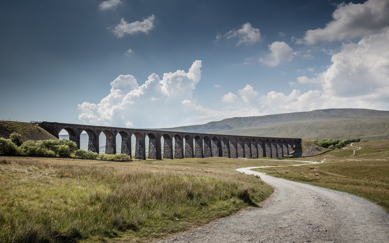 A long stone railway viaduct of many arches crossing open moorland beneath cloud